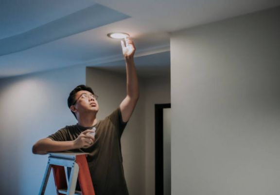 an asian chinese mid adult male changing light bulb in living room, apartment home